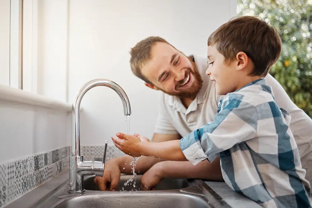 father helping son wash hands in kitchen sink